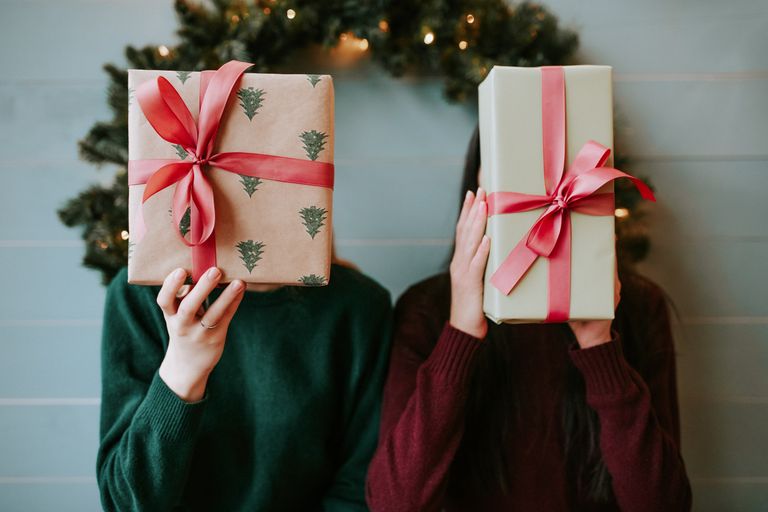 Twee mensen houden ingepakte kerstcadeaus voor hun gezicht.